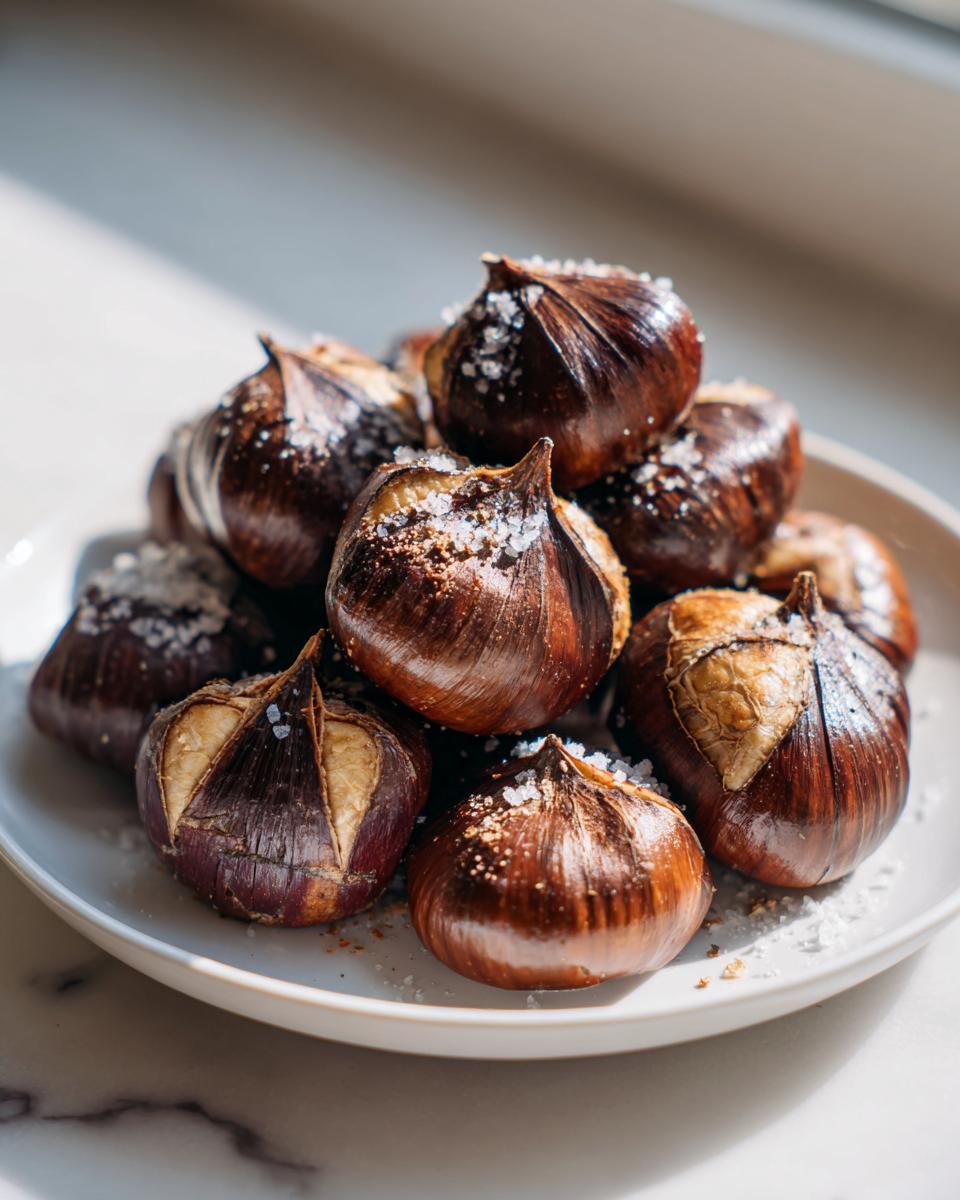 Een stapel geroosterde kastanjes met een zoutkristallen topping, klaar om gegeten te worden, als onderdeel van het recept voor Salt And Pepper Roasted Chestnuts.