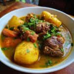 Close-up van een kom met rijke Sancocho Dominicano, vol met stukken vlees, gele aardappelen en verse peterselie.