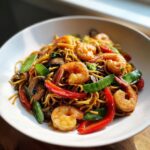 Close-up van een kom met heerlijke Shrimp Lo Mein, vol met garnalen, rode paprika, peultjes en champignons.
