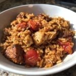 Close-up van een portie Slow Cooker Cajun Jambalaya met rijst, kipstukjes en cherrytomaten in een witte kom.