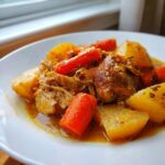 Close-up van een bord met Slow Cooker Chicken Stew, met malse kip, wortels en aardappelen in jus.
