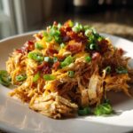 Een portie geraspte Slow Cooker Crack Chicken, gegarneerd met gesmolten kaas, krokant spek en lente-ui.