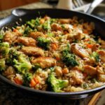 Close-up van een Chicken Rice Vegetable Skillet met stukjes kip, broccoli en wortel in een zwarte koekenpan.