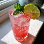 Een hoog glas met Strawberry Mint Sparkling Limeade, ijsblokjes, munt en een schijfje limoen.