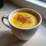 Close-up van een witte mok gevuld met een felgele Golden Milk Latte, afgetopt met kaneelpoeder.
