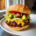 Close-up van een heerlijke California Burger met gesmolten kaas, avocado, tomaat en sla op een wit bord.