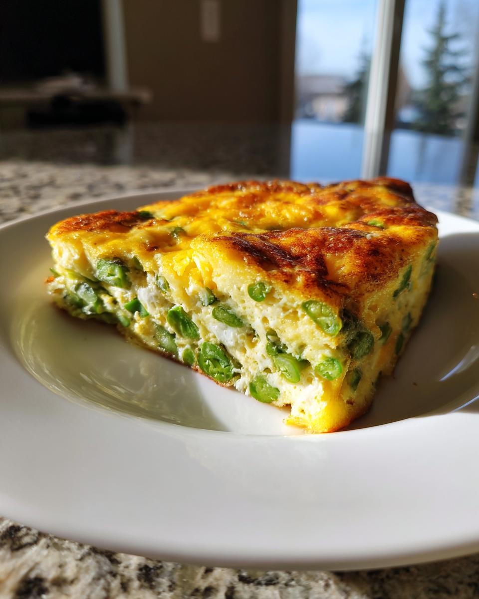 Een dikke, goudbruin gebakken portie Cheesy Asparagus Frittata met veel groene asperges op een wit bord.