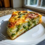Een driehoekig stuk Cheesy Asparagus Frittata met groene asperges en een goudbruine, kaasachtige bovenkant op een wit bord.