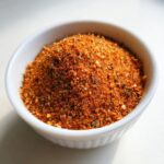 Close-up van een hoopje oranjerood Chicken Seasoning Blend in een klein wit kommetje.