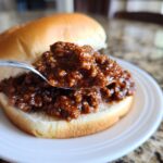 Een lepel met glanzende Dr Pepper Sloppy Joes vulling wordt boven een zacht broodje gehouden.