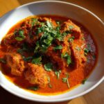 Close-up van een kom met romige, oranje Kip Tikka Masala, gegarneerd met verse koriander.