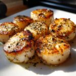 Close-up van zes perfect gegrilde Easy Grilled Scallops met kruiden en boter op een wit bord.