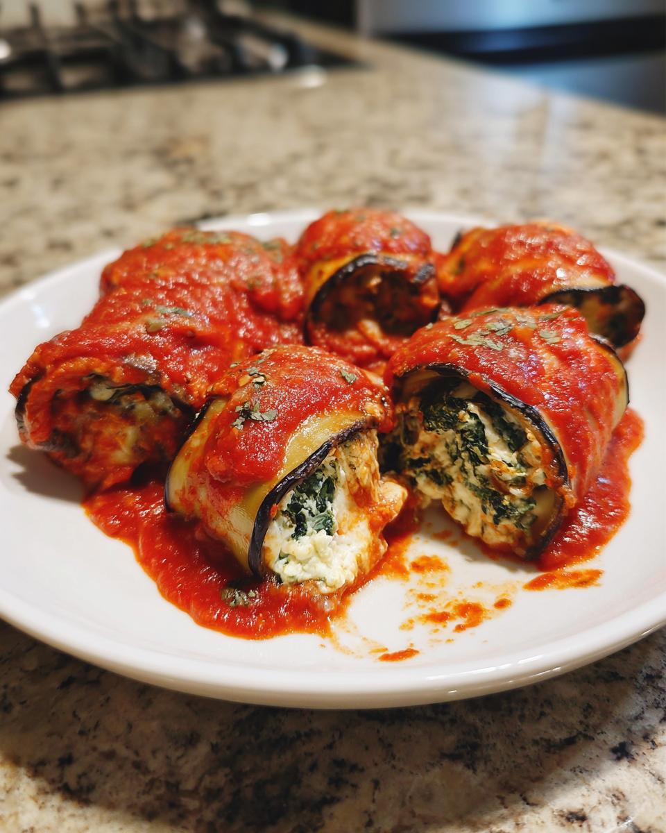 Drie Eggplant Rollatini gevuld met ricotta en spinazie, overgoten met rijke tomatensaus.