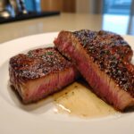 Twee dikke plakken sappige Garlic Guajillo Steak met een perfect medium-rare kern op een wit bord.