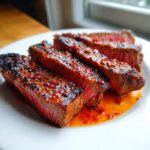 Drie dikke plakken sappige Garlic Guajillo Steak met een pittige, oranje glazuur op een wit bord.