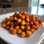 Een stapel goudbruine, gekruide geroosterde kikkererwten op een wit bord, klaar om gegeten te worden.