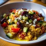 Close-up van een heerlijke Mediterranean Bowl met gele quinoa, komkommer, tomaat, olijven en feta.