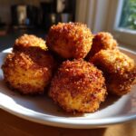 Close-up van een stapel goudbruine, krokante Potato Croquettes op een wit bord, badend in zonlicht.