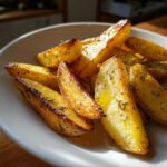 Close-up van goudbruine, gekruide Griekse citroenaardappelen geserveerd op een witte schaal.