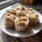 Close-up van zes vers gestoomde Shrimp Shumai dumplings op een wit bord, klaar om te eten.