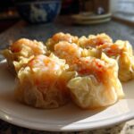 Close-up van zes gestoomde Shrimp Shumai met een stukje garnaal bovenop, geserveerd op een witte schotel.