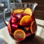 Een karaf met een rijke, rode Sangria Recipe, gevuld met ijsblokjes, sinaasappelschijfjes en stukjes fruit.
