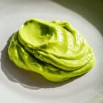 Close-up van een klodder felgroene, gladde Lichte Romige Avocado Limoen Saladedressing op een lichtgrijs bord.