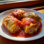 Drie smakelijke Macedonische Koolrolletjes geserveerd op een witte schotel met rijke tomatensaus.