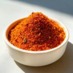 Close-up van een hoopje helderoranje Chicken Seasoning Blend in een kleine witte kom.