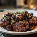 Drie stukken malse kip bedekt met een donkere, glanzende saus en pruimen, gegarneerd met bieslook voor de Easy Chicken Marbella.