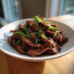 Close-up van malse Beef Bulgogi, gegarneerd met lente-ui en sesamzaadjes in een witte kom.