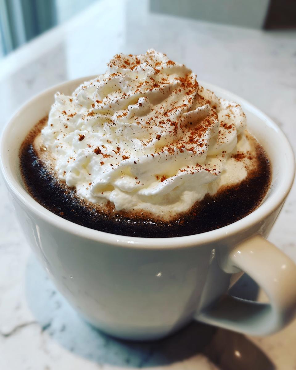 Close-up van een witte mok gevuld met donkere Mexicaanse Koffie, getopt met een royale toef slagroom en kaneel.