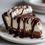 Een groot stuk romige Mississippi Mud Pie met een donkere koekjesbodem, overgoten met chocoladesaus en slagroom.