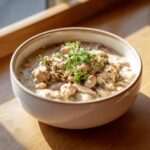 Close-up van een kom met romige White Chicken Chili, gegarneerd met witte bonen en verse tijm.