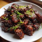 Close-up van een bord met glanzende, gekarameliseerde Panda Express Teriyaki Kip, bestrooid met sesamzaadjes en lente-ui.