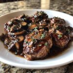 Dichtbij foto van malse Pork Marsala medaillons bedekt met een donkere saus en gesneden champignons, gegarneerd met peterselie.