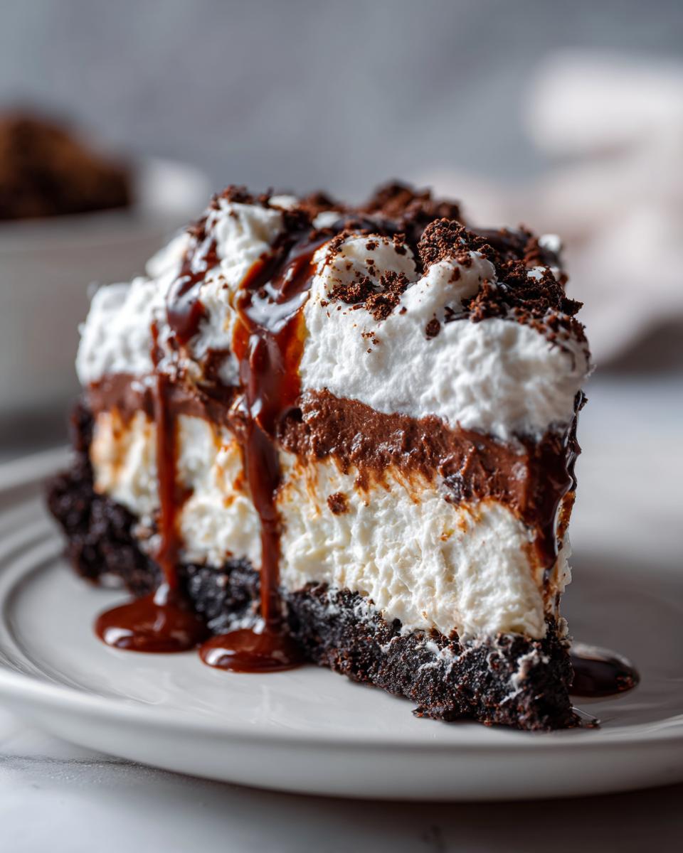 Een dikke, gelaagde snee Mississippi Mud Pie met chocolade, slagroom en chocoladesaus op een wit bord.