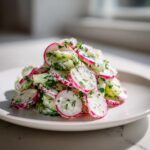 Een bergje Radijs Komkommer Salade met Knoflook Yoghurt Dressing, mooi opgemaakt op een wit bord.