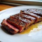 Gesneden Ribeye Steak Dinner, perfect medium-rare met een gekruide korst en jus op een wit bord.