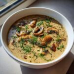 Close-up van een kom romige Hungarian Mushroom Soup, gegarneerd met gebakken champignons en verse dille.