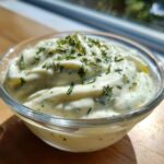 Close-up van romige, lichte Ranch Dressing Recipe gegarneerd met verse groene kruiden in een glazen kom.
