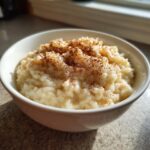 Een kommetje romige rijstepap, rijkelijk bestrooid met kaneel, gefotografeerd in natuurlijk licht.