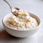 Een lepel met romige rijstpudding wordt uit een witte kom getild.