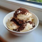 Drie bollen romige Tiramisu Ice Cream in een witte kom, bestrooid met cacaopoeder.