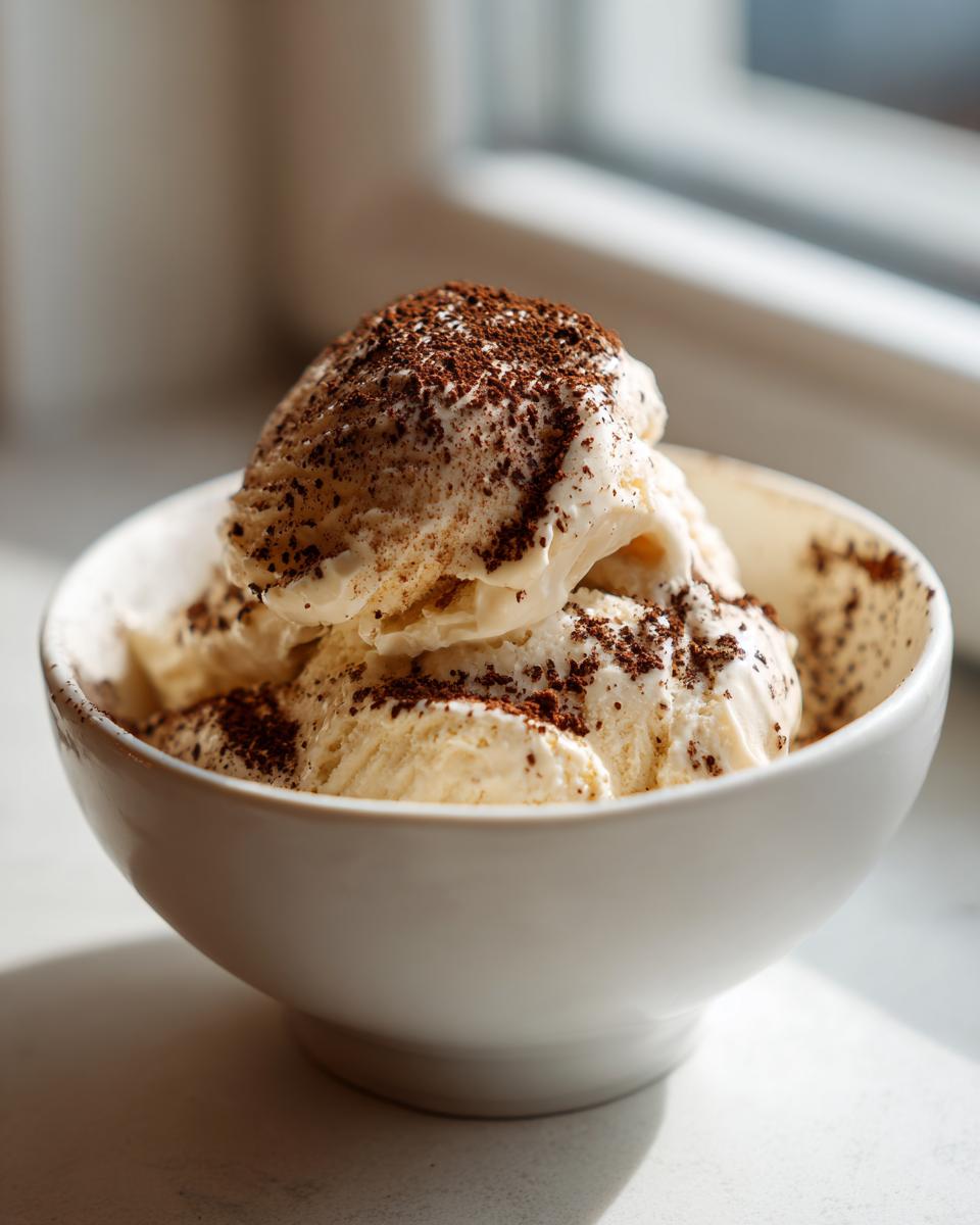 Drie bollen romige Tiramisu Ice Cream in een witte kom, bestrooid met cacaopoeder.