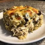 Een portie Salsa Verde Chicken Rice Casserole met gesmolten kaas en zwarte bonen op een wit bord.