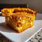 Een close-up van een vierkant stuk Pumpkin Blondies met stukjes witte chocolade op een wit bord.