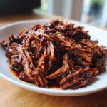 Close-up van sappig, uit elkaar getrokken Slow Cooker Beef Barbacoa op een witte schaal.