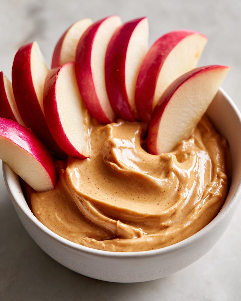 Een kom romige Toffee Apple Dip met schijfjes rode appel erin gedoopt.