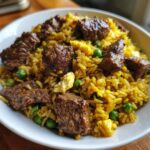 Close-up van een witte kom gevuld met gele Steak Fried Rice, stukjes rundvlees, doperwten en roerei.